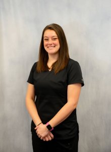 Studio portrait of Dr. Melany Leek smiling in dark scrubs against a grey backdrop