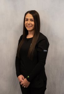 Studio portrait of a smiling female staff member with long dark hair wearing a black long-sleeve scrub top