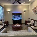 View from the sofa facing a large curved fish tank in a modern dental office waiting area.