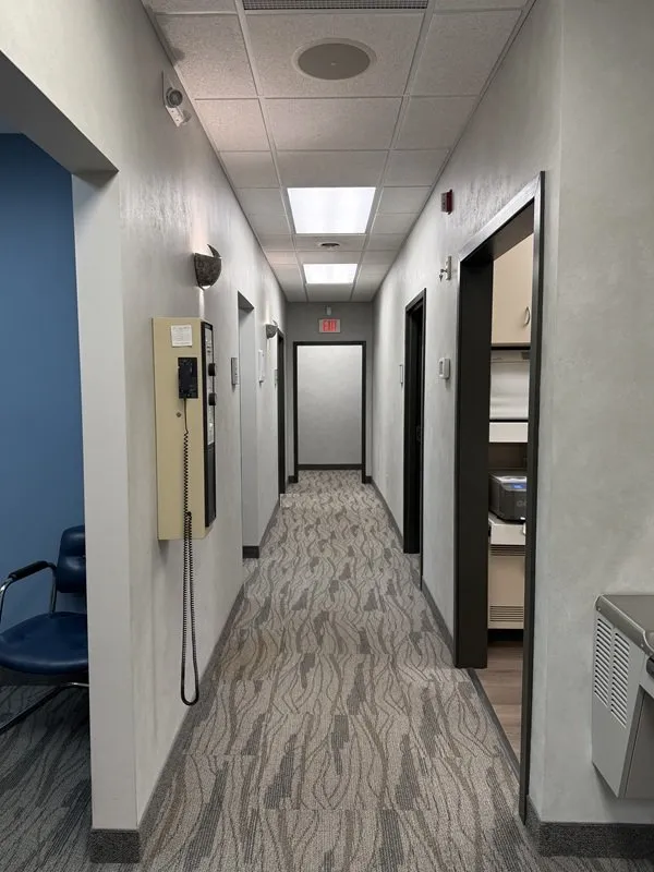 Long hallway inside a dental clinic with carpeted flooring, white walls, recessed ceiling lights, and doors leading to treatment rooms