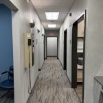 Long hallway inside a dental clinic with carpeted flooring, white walls, recessed ceiling lights, and doors leading to treatment rooms
