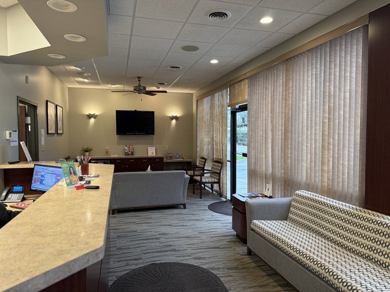 Reception and waiting area showing the front check-in counter, seating sofa, television, and window blinds