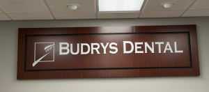 Wall sign displaying BUDRYS DENTAL with a toothbrush logo on a dark wood background